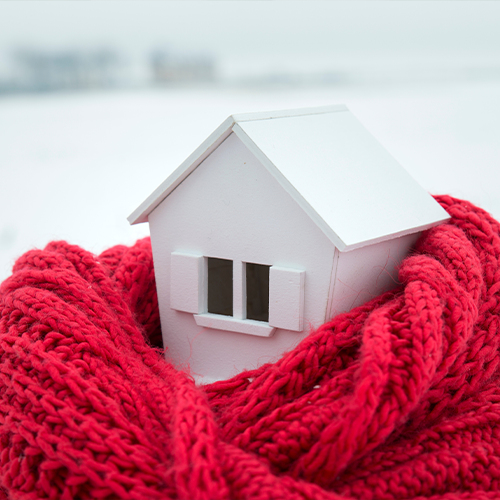 Small model of a house wrapped in a red knitted scarf