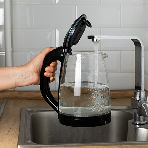 Person filling kettle with water from the kitchen tap